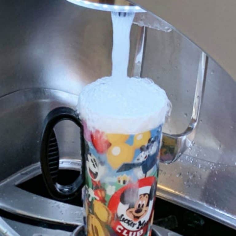 Disney refillable mug overflowing as it is being refilled at a stainless steel freestyle coke machine.