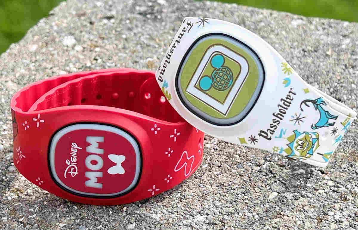 Two Disney magic bands resting on a stone - one is red and says 'Mom', the other is cream and says 'Passholder'