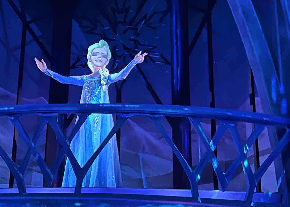 Animatronic Elsa from Frozen in her long blue dress standing on a dark balcony singing 'Let It Go'