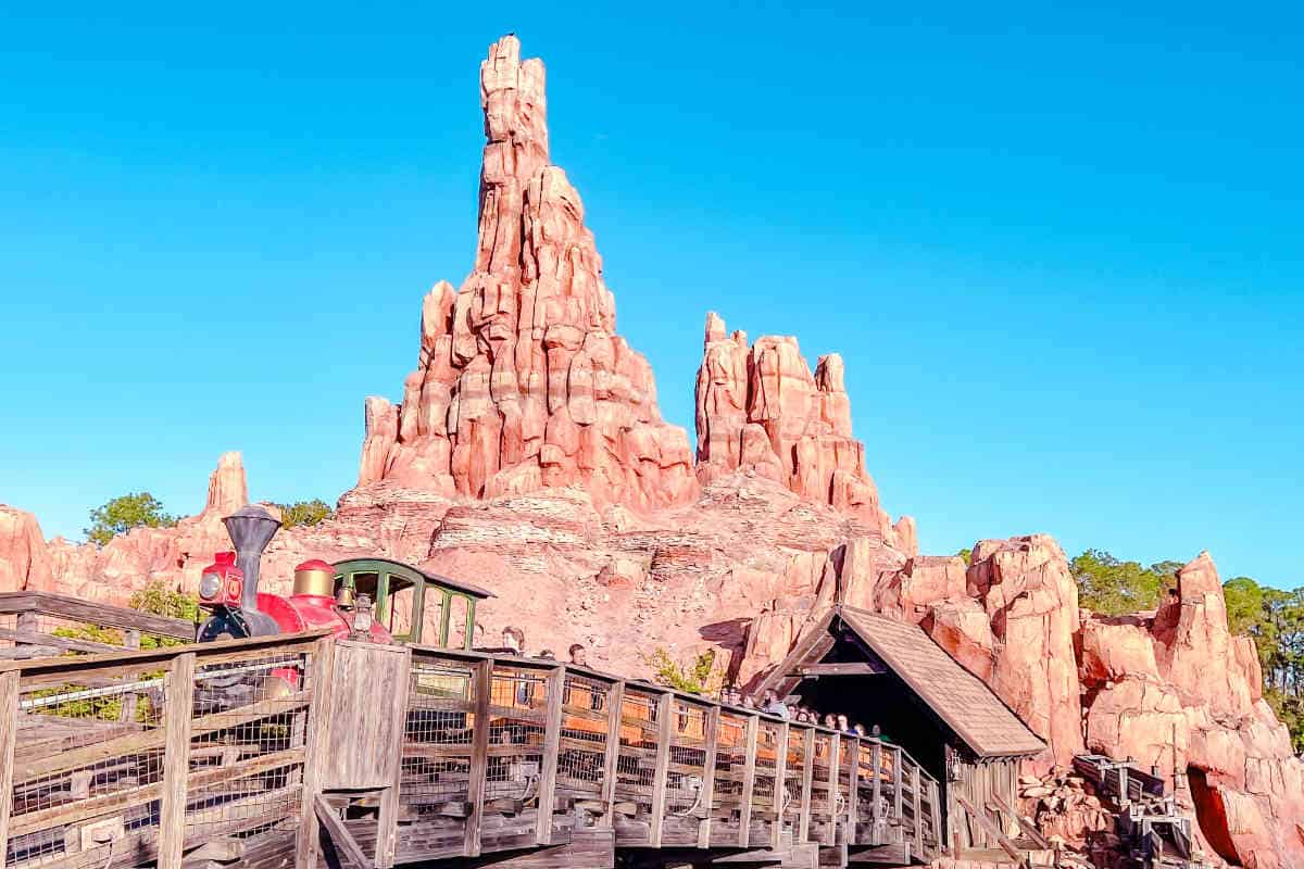 Mine train ride at Magic Kingdom with a red lead car on a wooden track in front of a red rock mountain