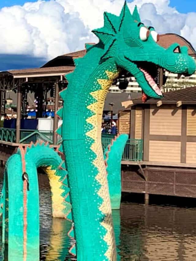 Green and beige Loch ness creature made from Legos in the lagoon at Disney Springs in front of several brown and beige buildings