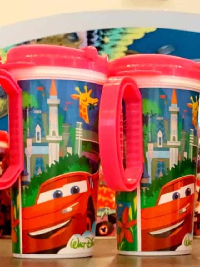 A group of insulated travel mugs sitting on a shelf; pink or black and handles with Mickey Mouse designs on the bottom of the cup.
